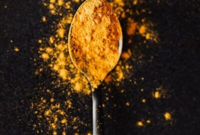 Photo d'illustration - From above of creative composition of bright ground turmeric on metal tablespoon spilled on black table